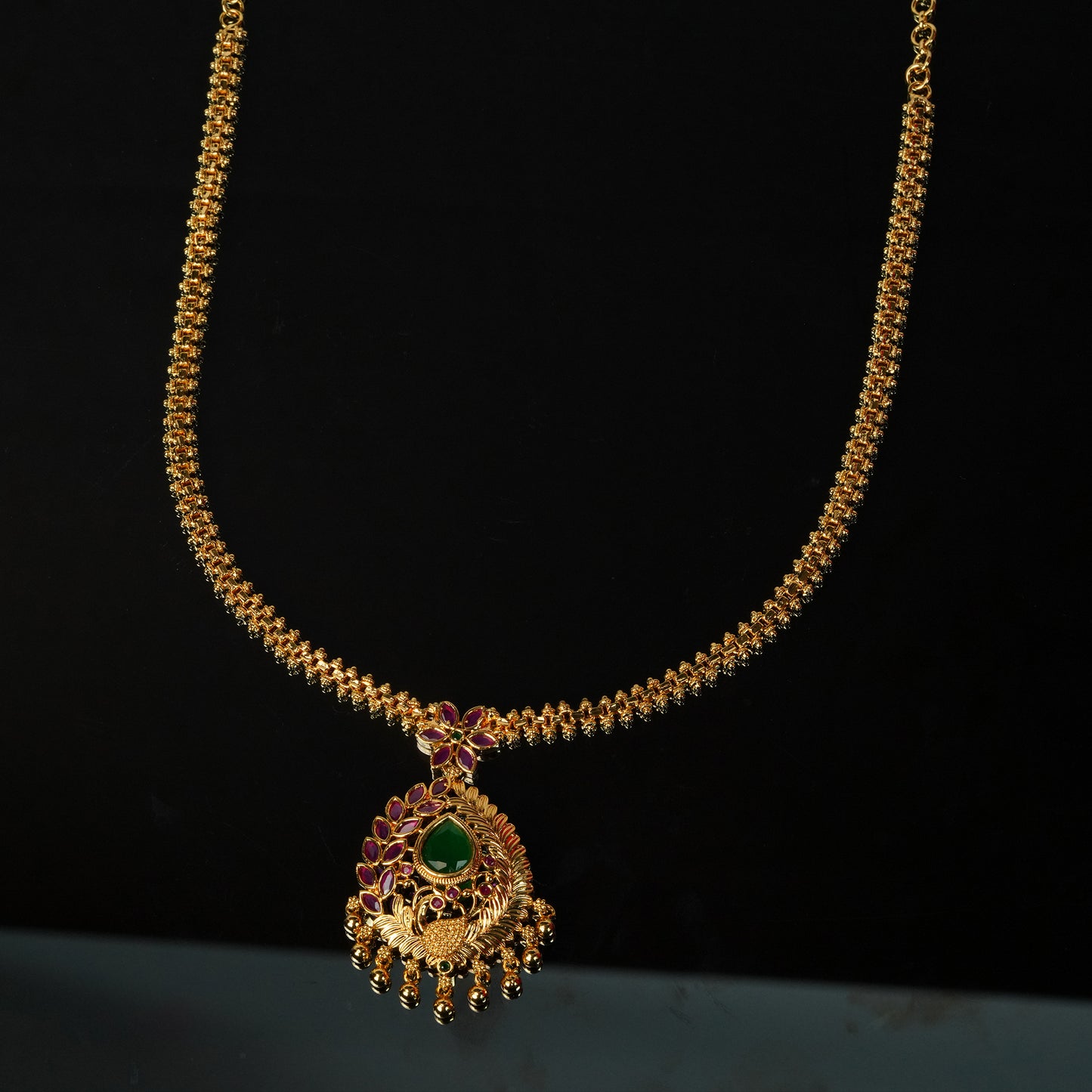 Gold necklace with intricate design, featuring a central green gemstone and purple accents.