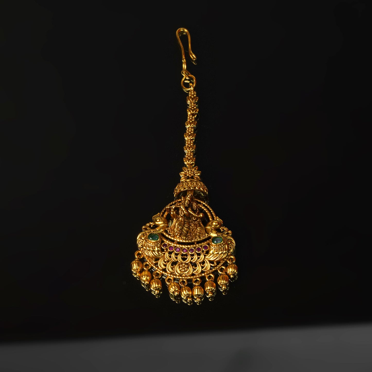 A single ornate gold earring with intricate designs, featuring small dangling beads and colorful gemstones.
