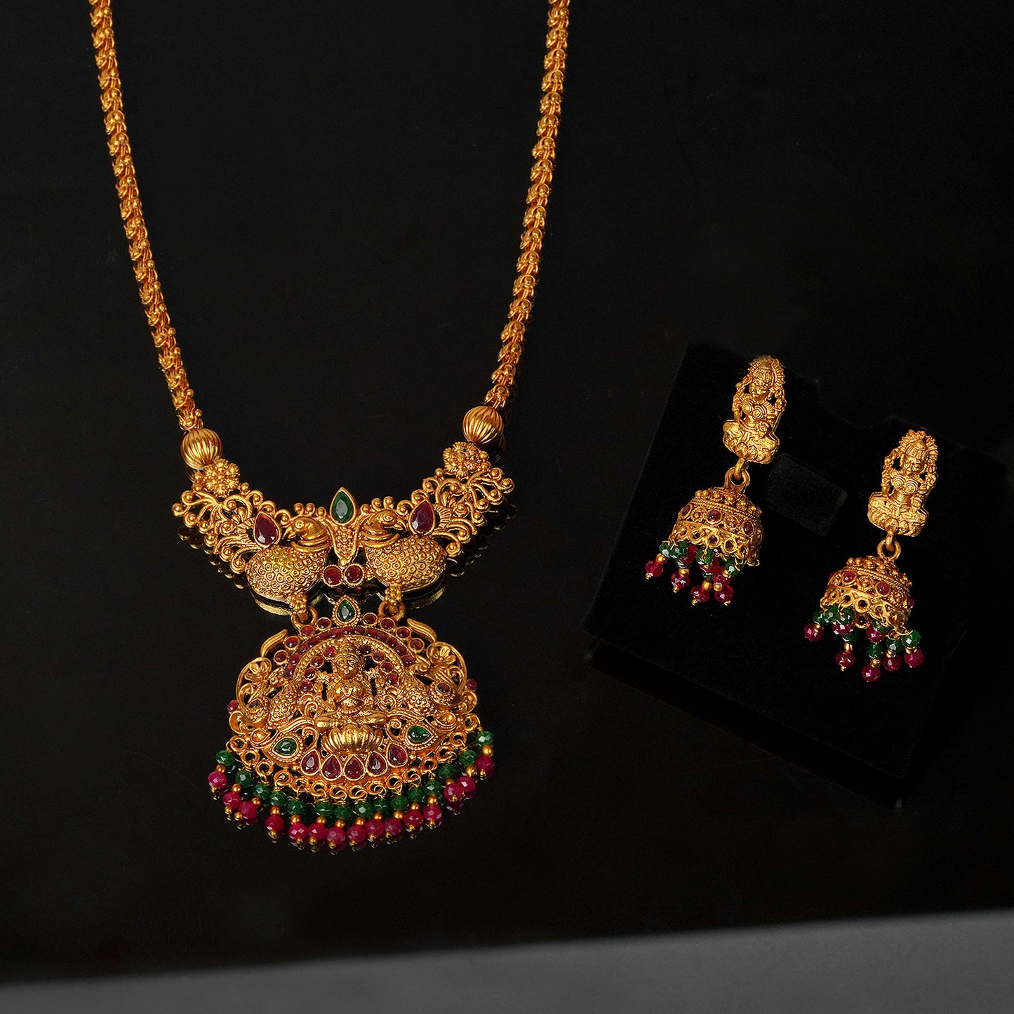 Gold necklace with intricate design and matching earrings adorned with red and green gemstones.