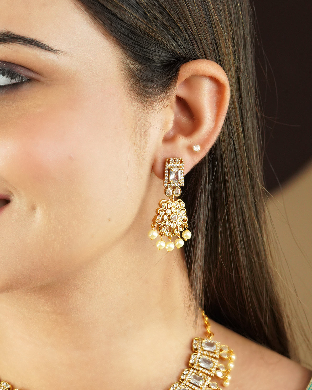 A close-up of a woman's ear wearing a gold earring with intricate design and pearl accents.