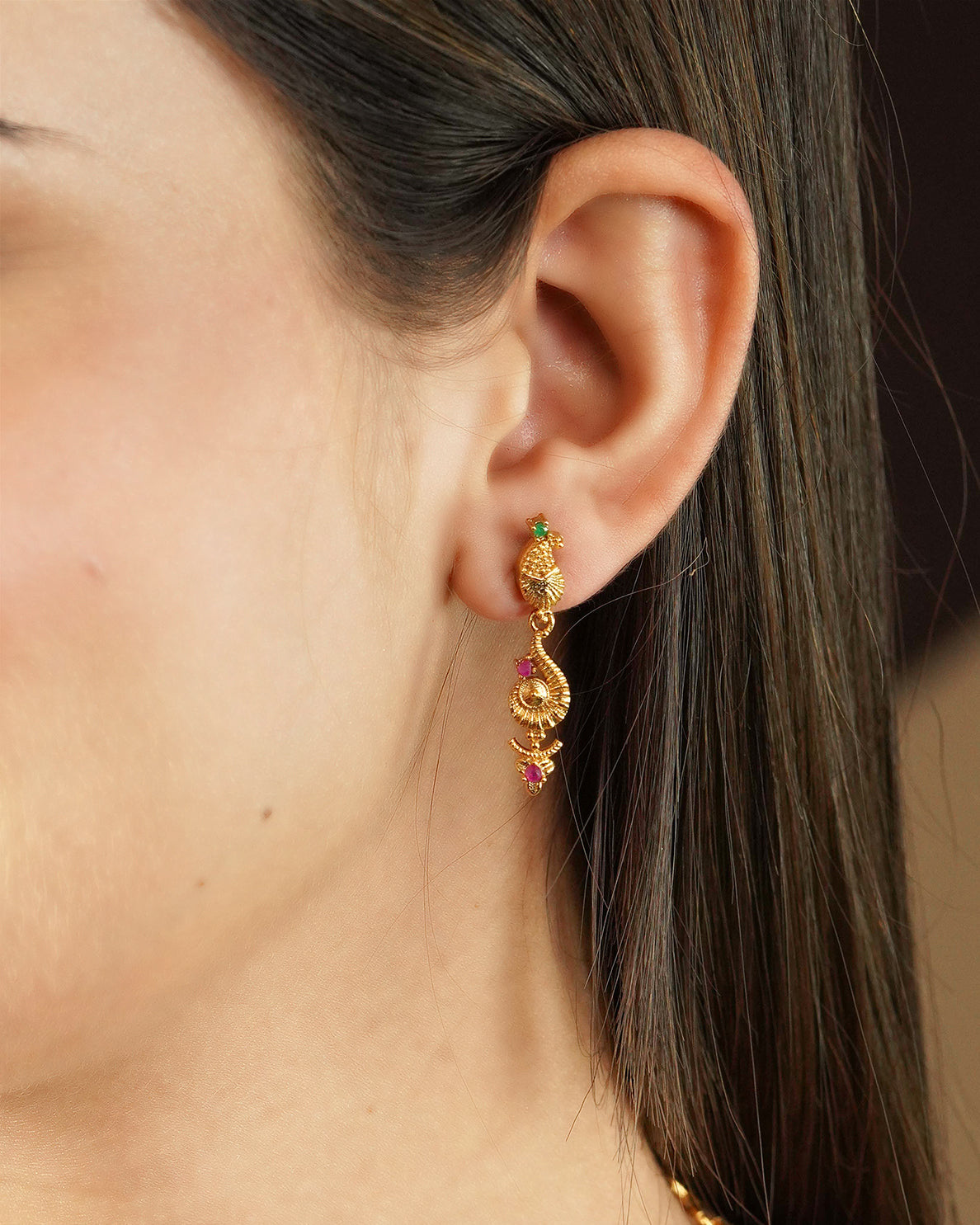 Close-up of a woman's ear wearing a gold earring with intricate design and colorful gemstones.