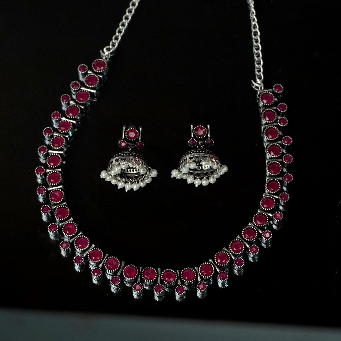 A silver necklace and matching earrings set with red gemstones and intricate detailing.