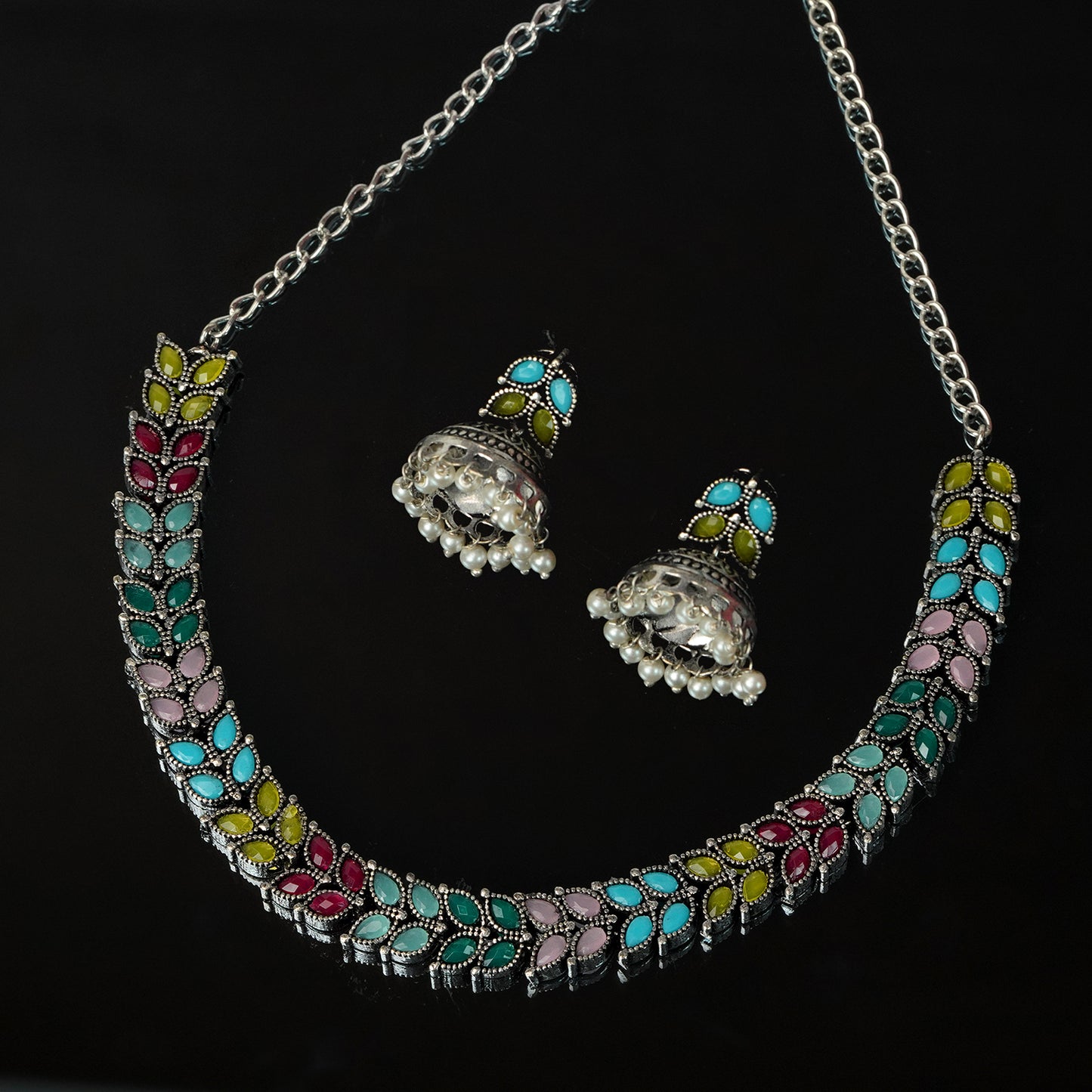 A colorful necklace and matching earrings set with intricate floral designs in blue, pink, yellow, and green. The necklace features a chain and the earrings have a bell-shaped design with small white beads.