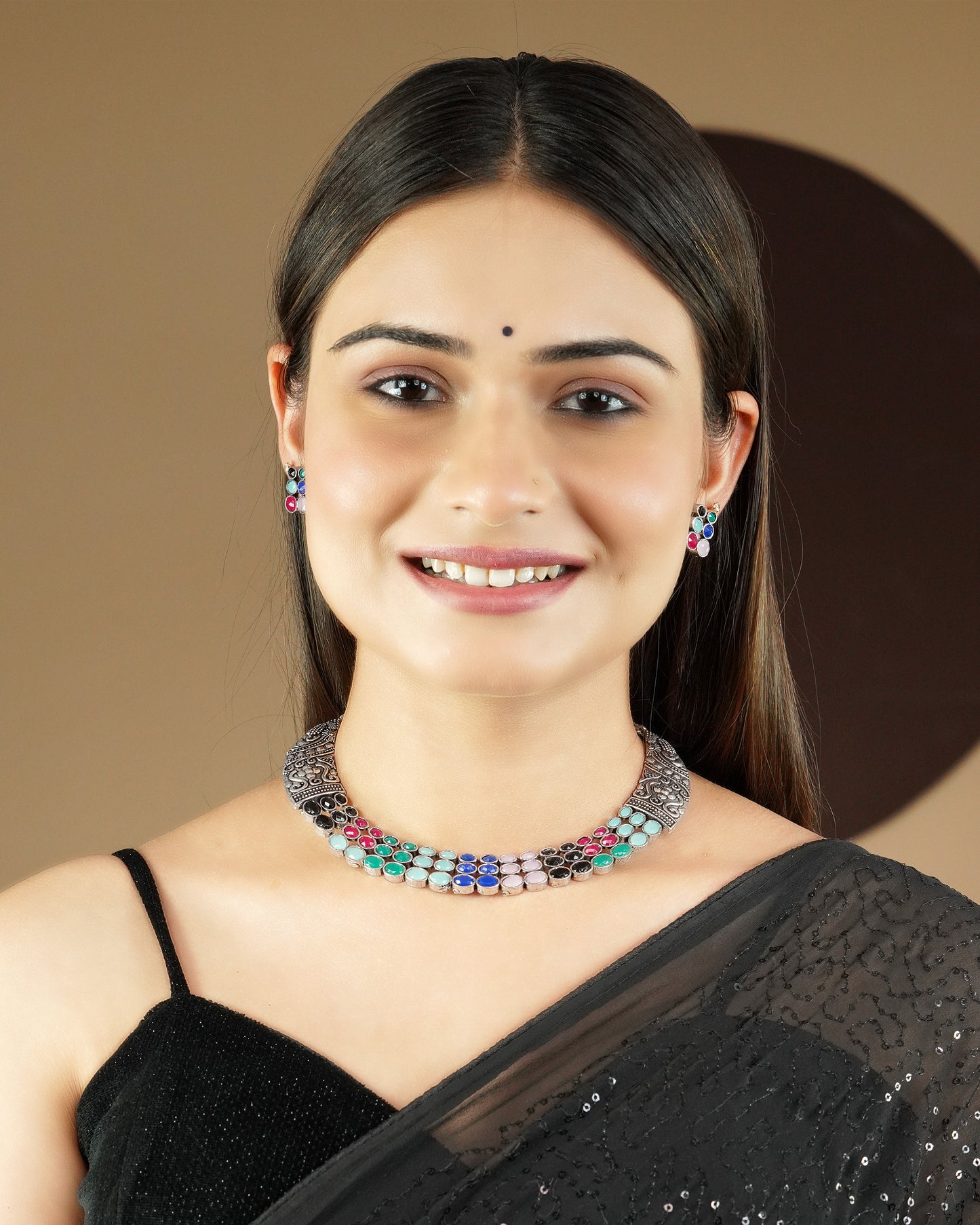 A woman wearing a black saree and a colorful beaded necklace with matching earrings.