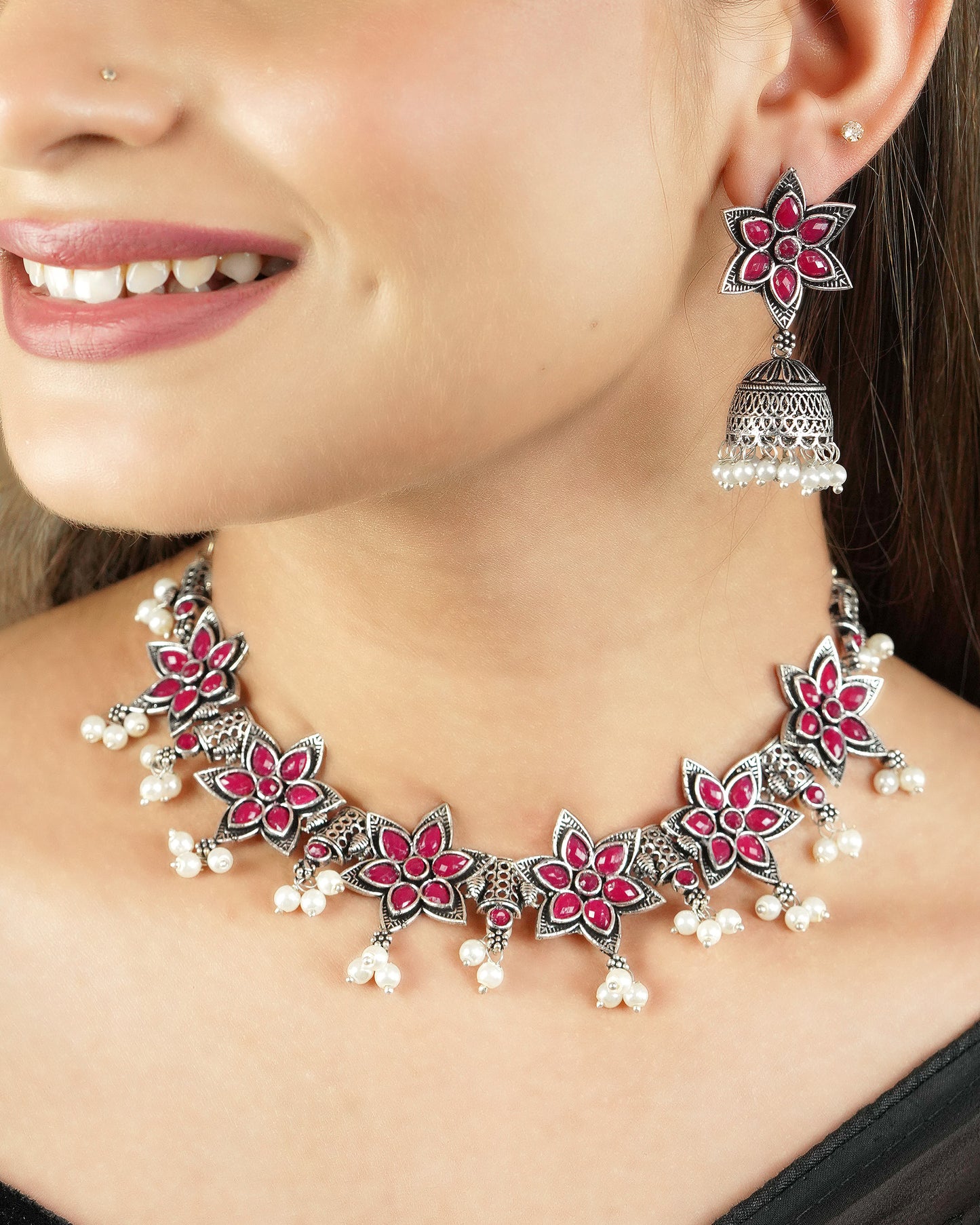 A woman wearing a floral necklace and matching earrings with red and white accents.