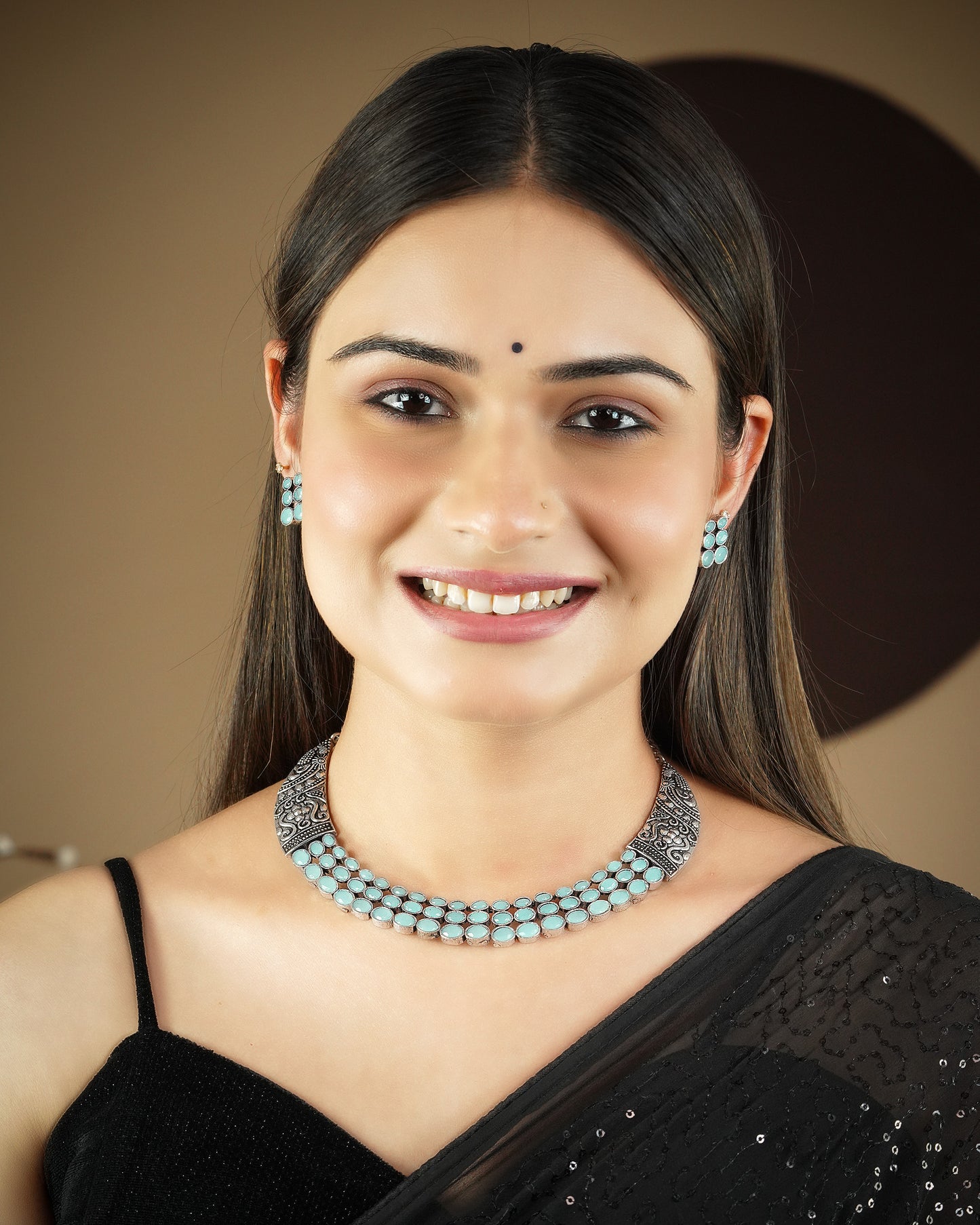 A woman wearing a black saree, a silver and turquoise necklace, and matching earrings.