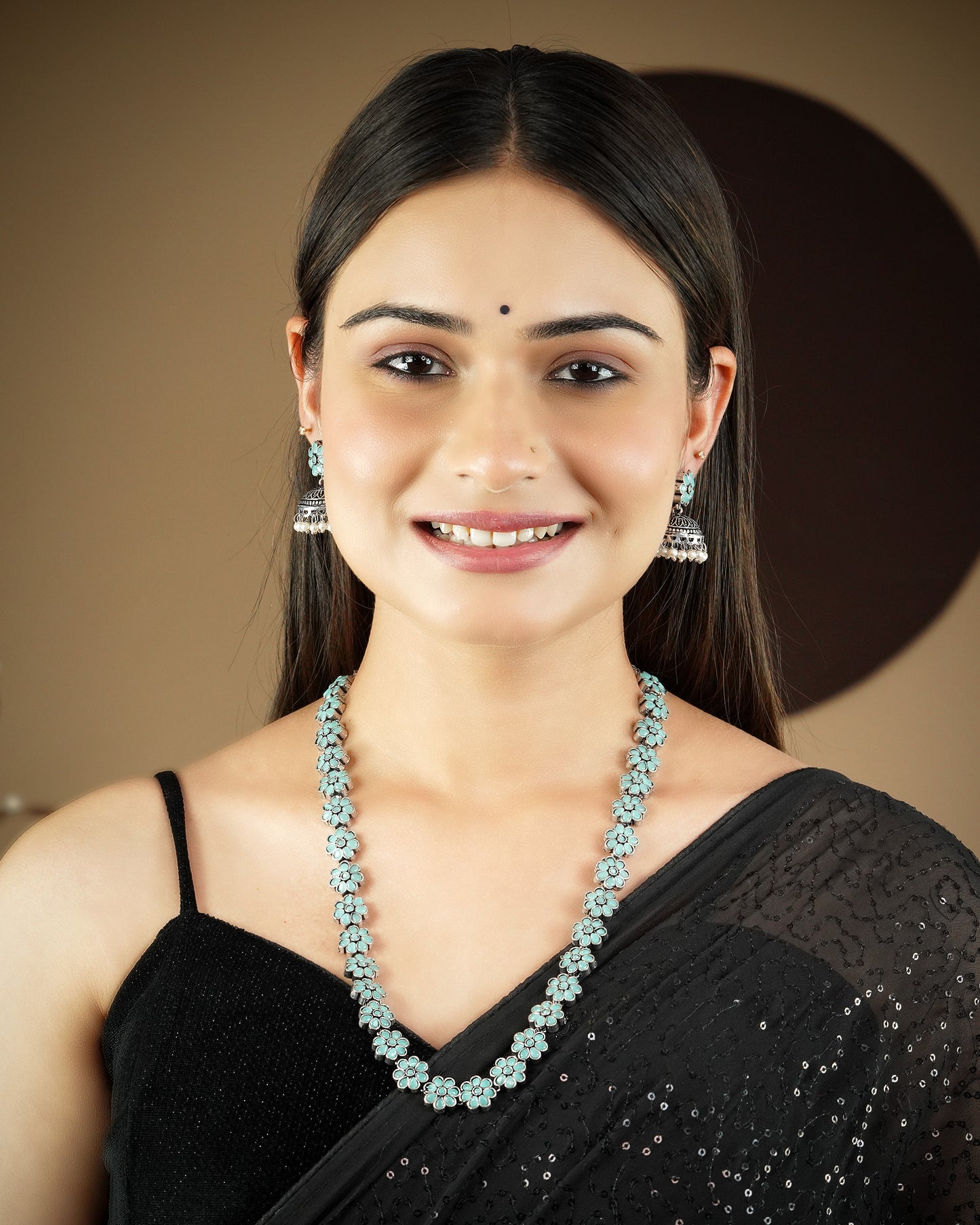 A woman wearing a black saree, a light blue floral necklace, and matching earrings.