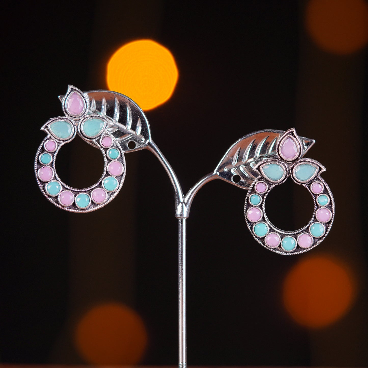 Silver earrings with pink and blue gemstones in a circular design, featuring leaf-shaped accents at the top.