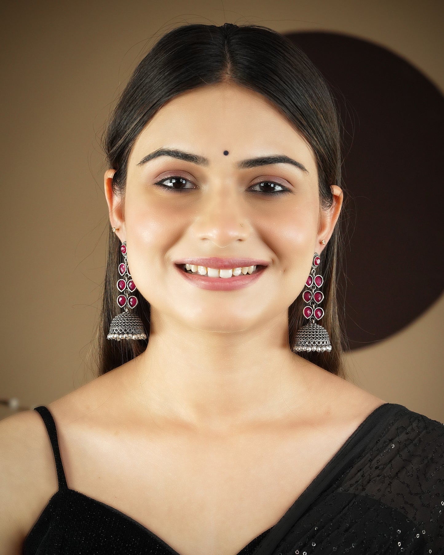 A woman wearing traditional silver jhumka earrings with pink gemstones and a black saree.