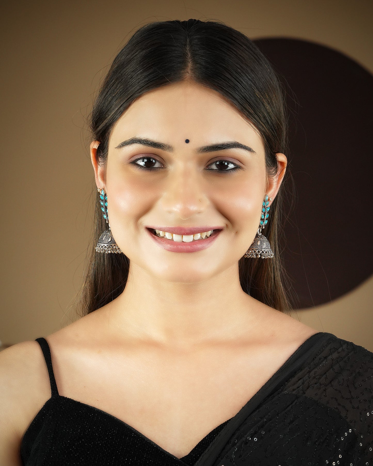 A woman wearing a black saree and silver jhumka earrings, smiling.