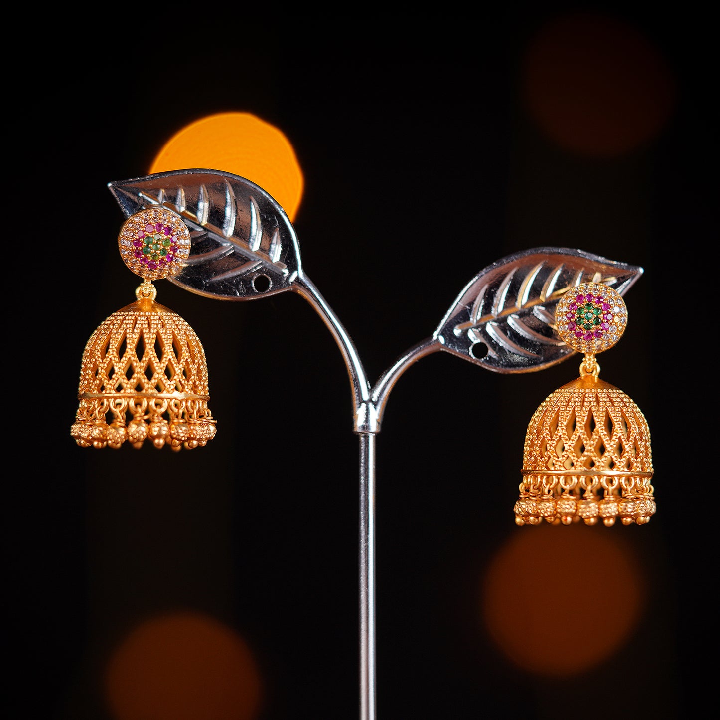 A pair of gold jhumka earrings with intricate lattice design and pink gemstone accents.