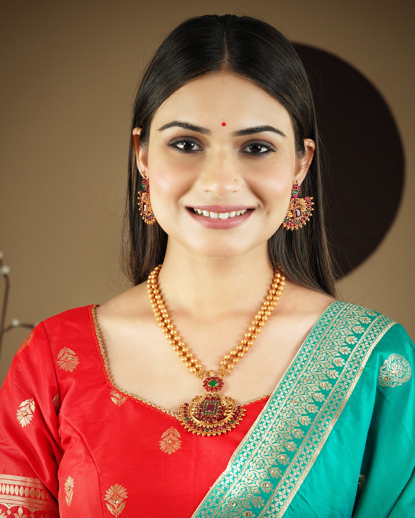 A woman wearing a red and green traditional outfit, adorned with gold and red earrings and a matching necklace.