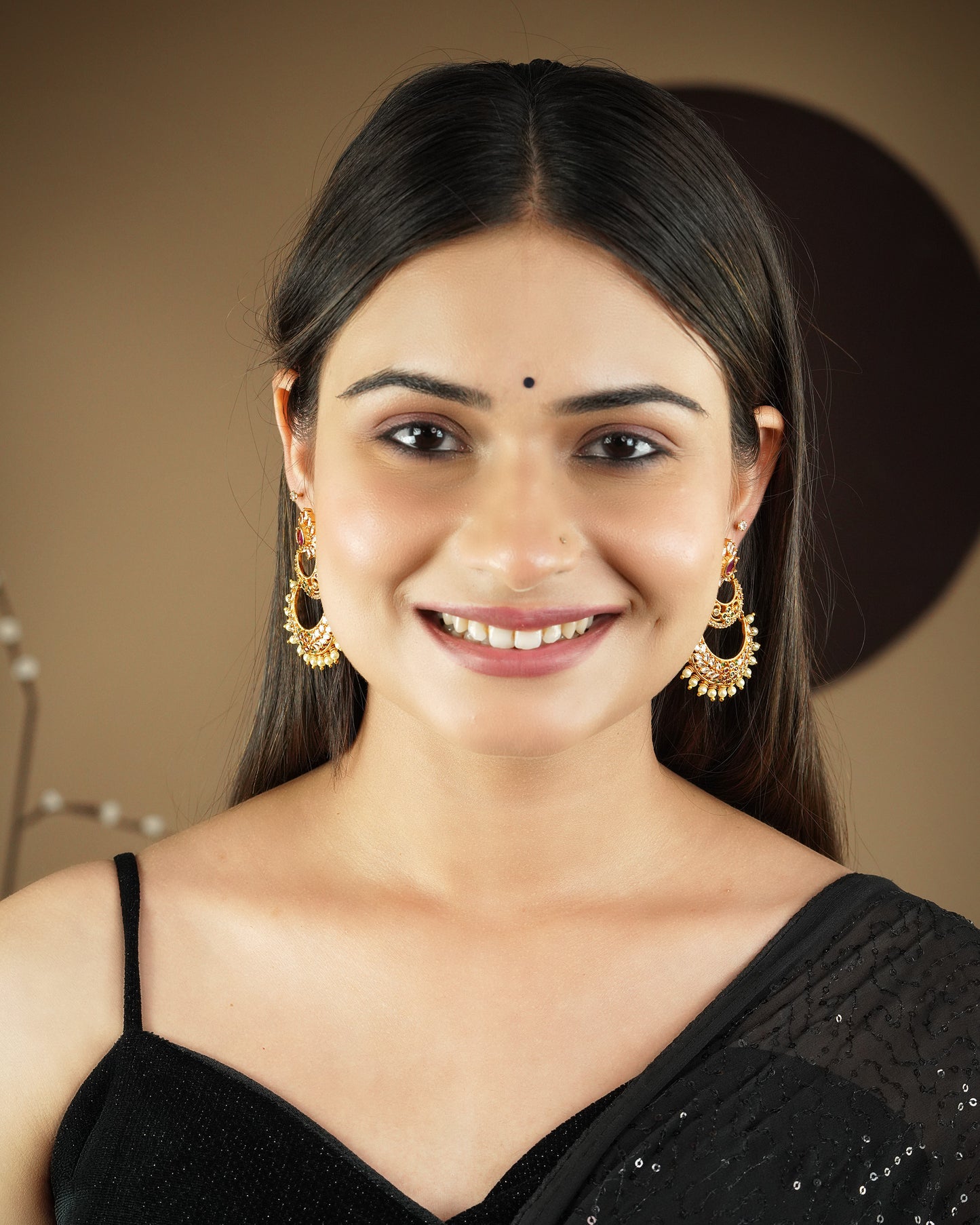 A woman wearing gold and black earrings and a black sleeveless top smiles at the camera.
