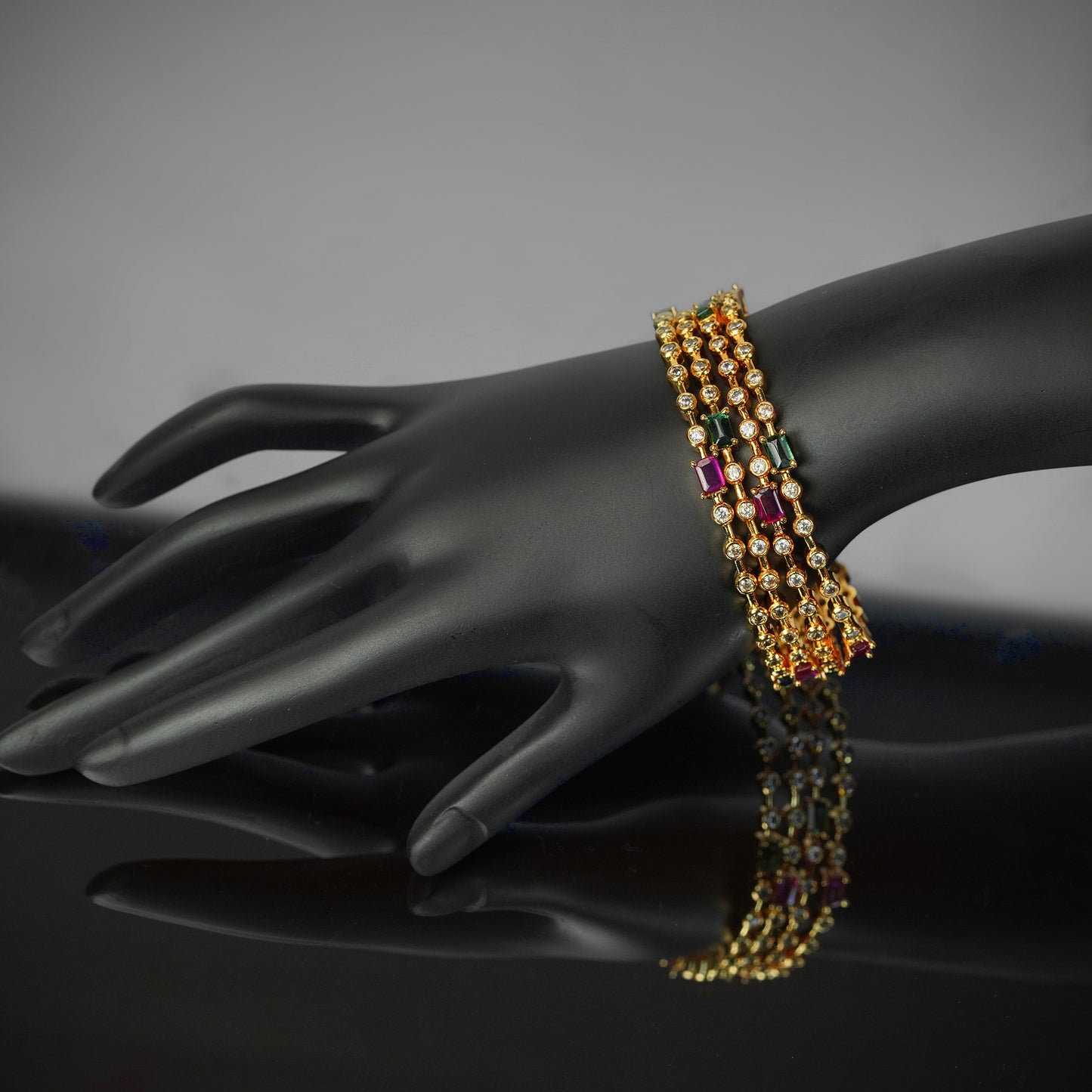 A gold bracelet with colorful gemstones displayed on a black mannequin hand.