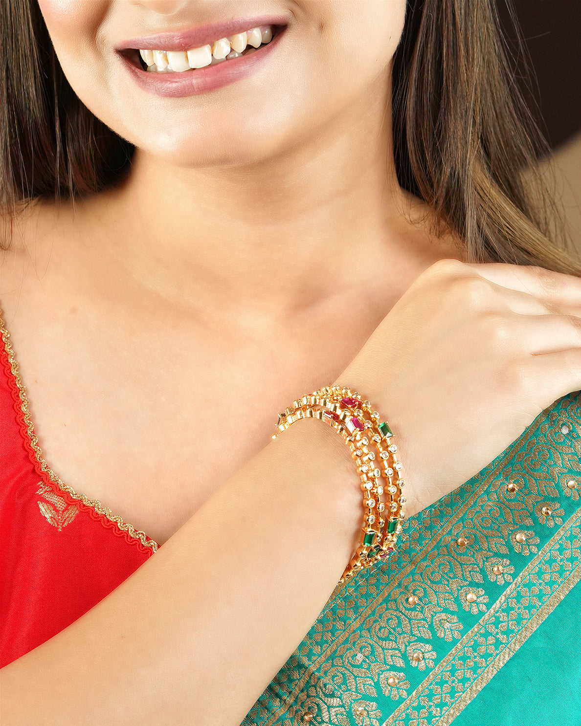 A woman wearing a red and green traditional outfit, showcasing a set of gold and multicolored beaded bangles on her wrist.