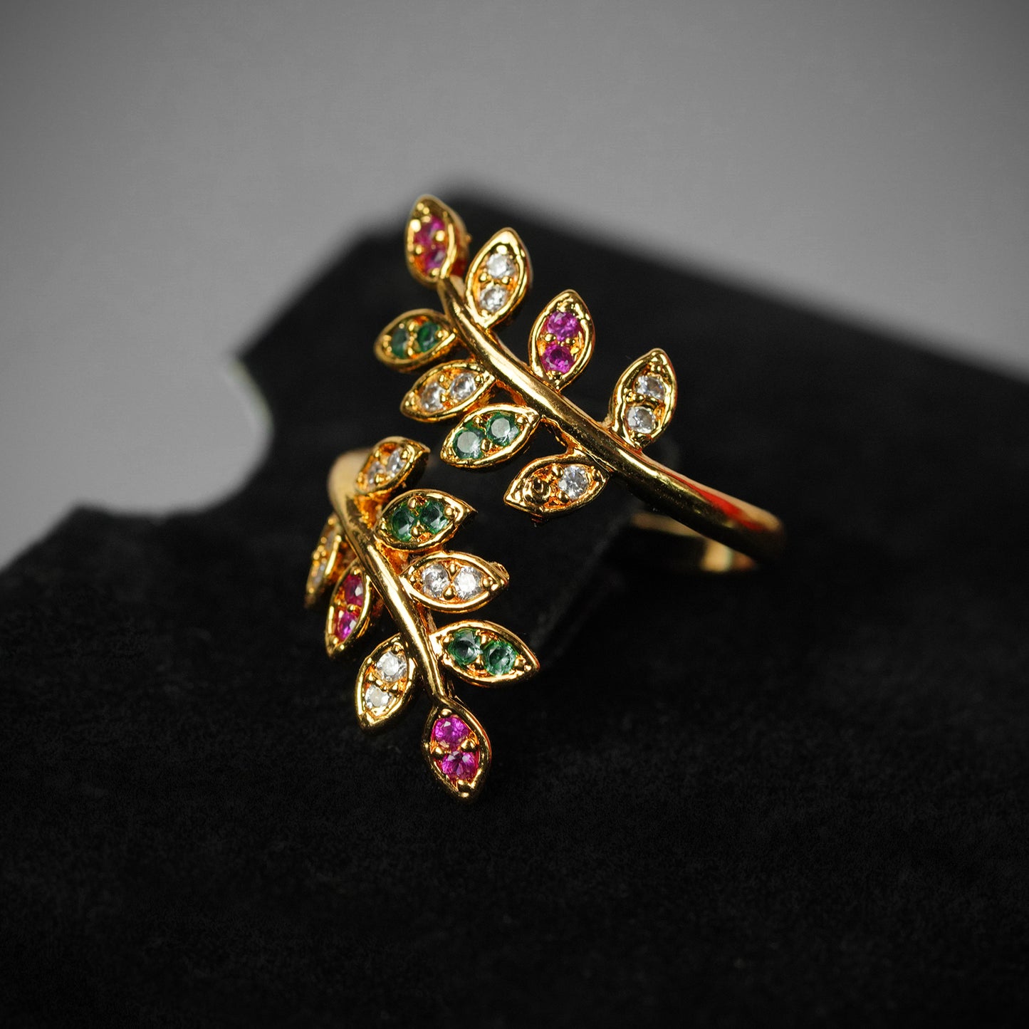 Gold ring with a leaf design, adorned with multicolored gemstones.