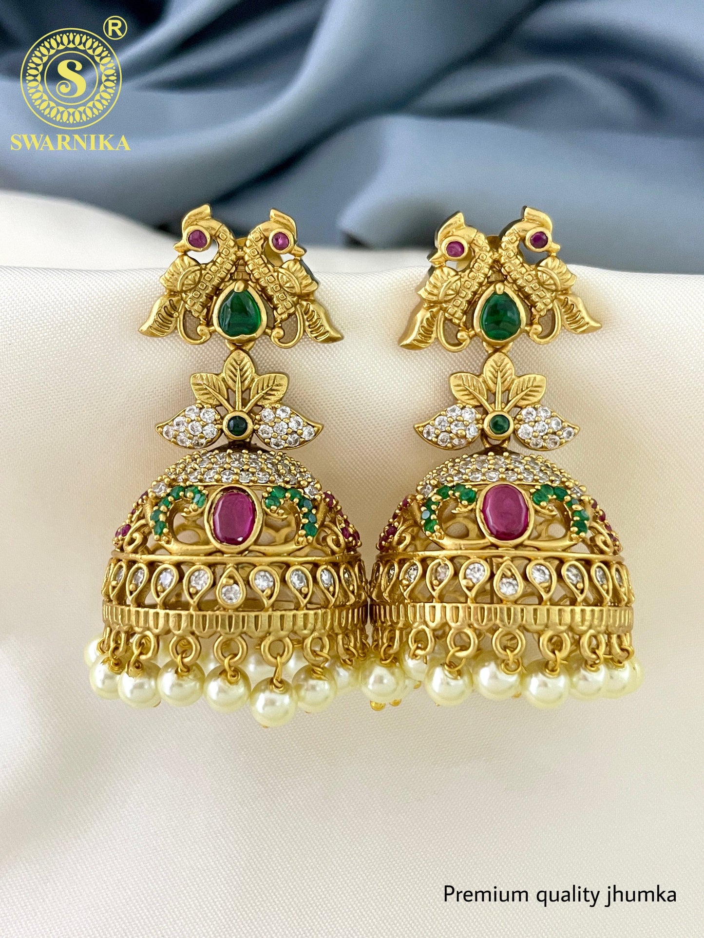 Gold jhumka earrings with intricate designs, featuring green and pink gemstones, and pearl drops.