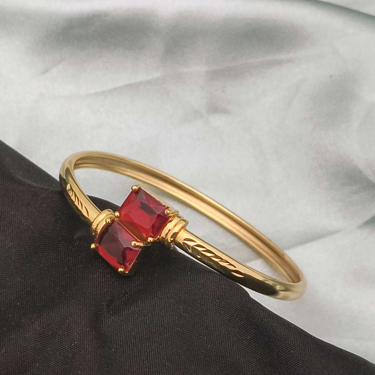 A gold bracelet featuring two square red gemstones.