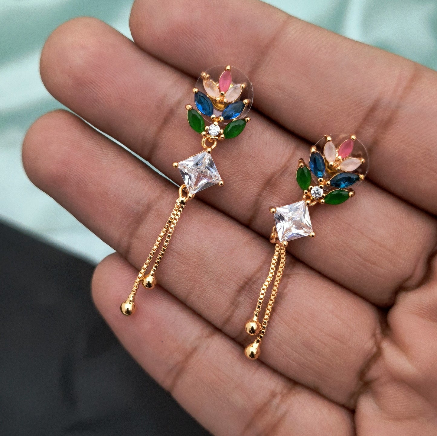 A pair of gold earrings featuring colorful gemstones and dangling chains.