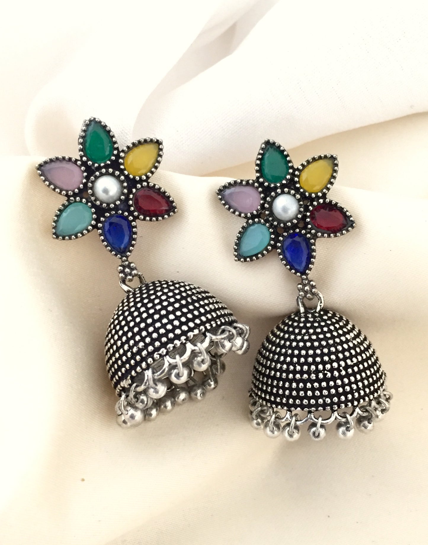A pair of silver jhumka earrings with intricate detailing and colorful floral tops.