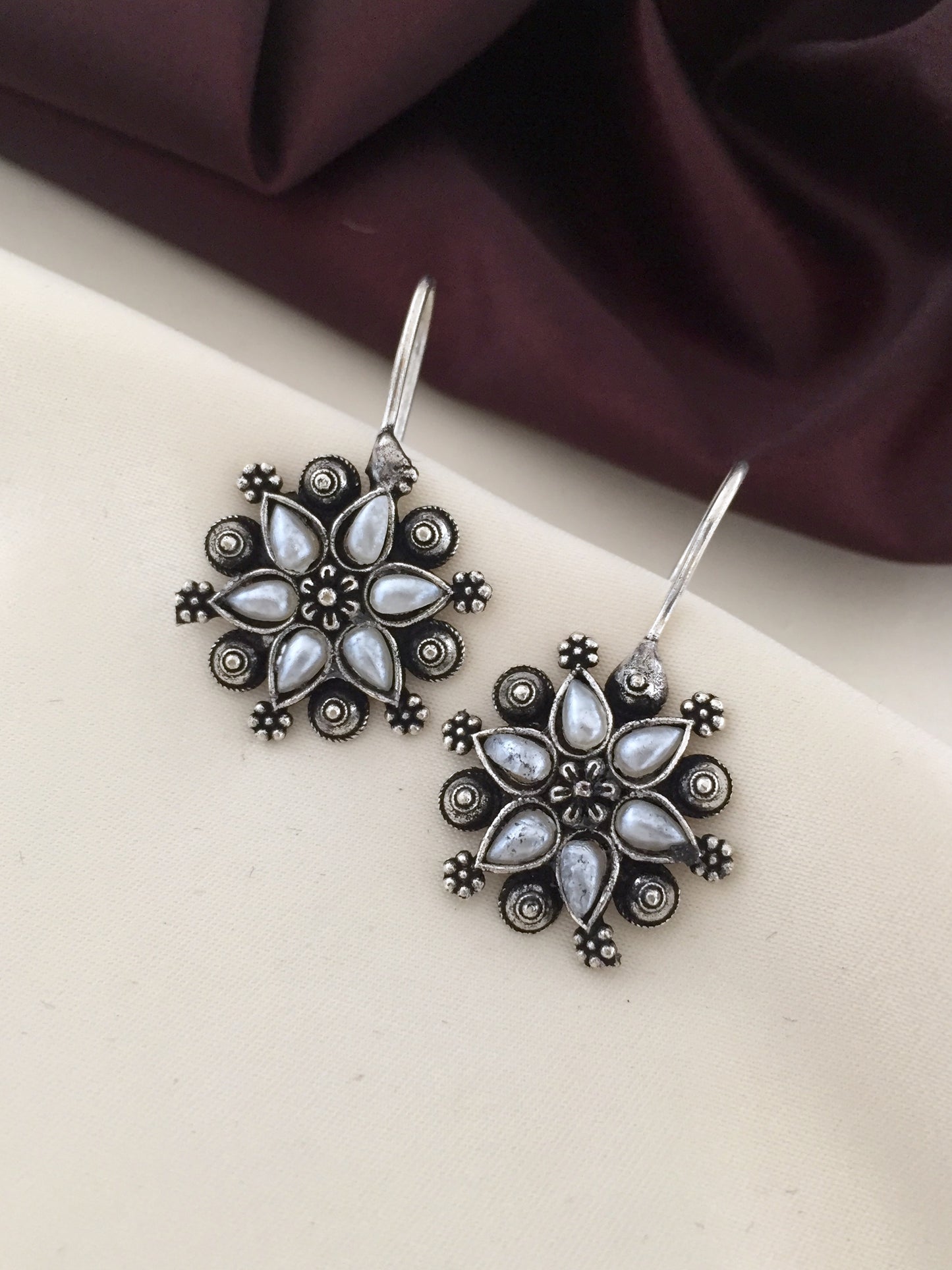 A pair of silver floral earrings with intricate detailing and white gemstone accents.
