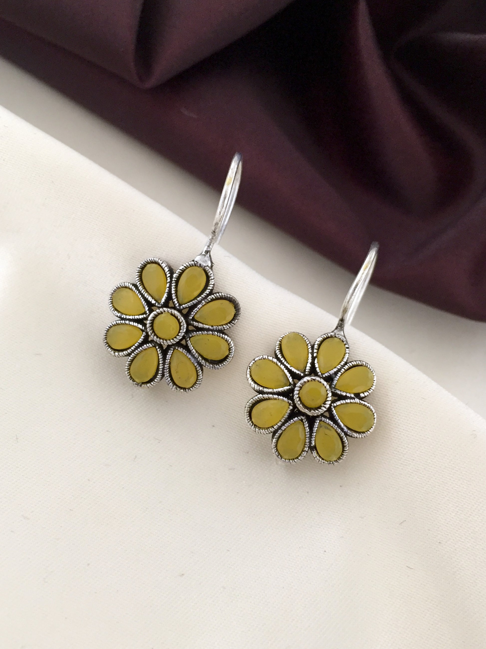 A pair of yellow flower-shaped earrings with silver accents and hook closures.