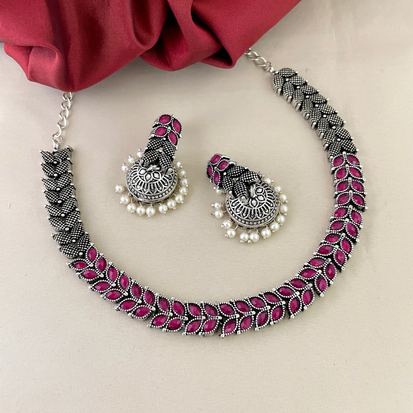 A silver necklace with pink gemstone accents and matching earrings adorned with pearls.