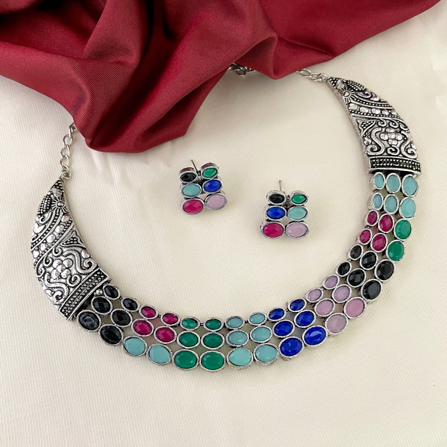 A silver necklace with intricate designs and colorful gemstones, accompanied by matching earrings.