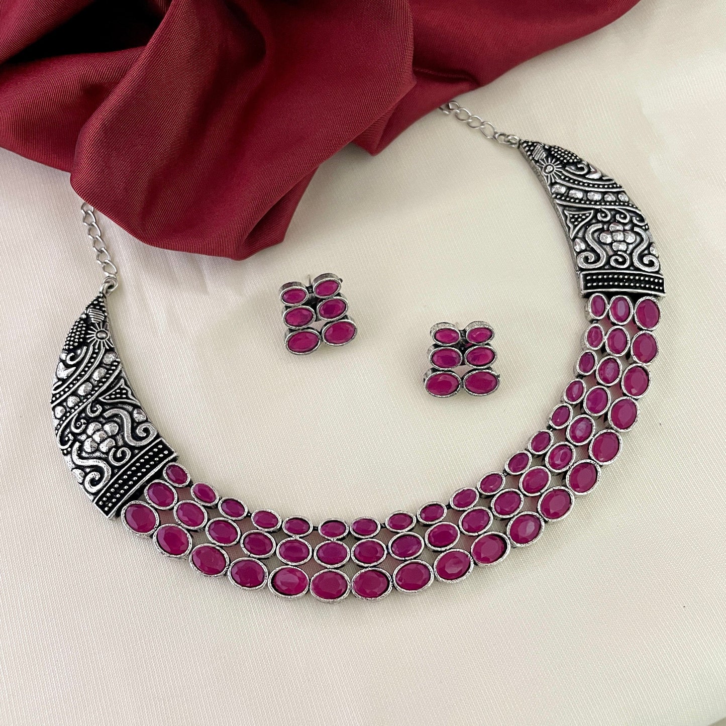 Silver necklace with intricate designs and multiple rows of pink stones, accompanied by matching pink stone earrings.