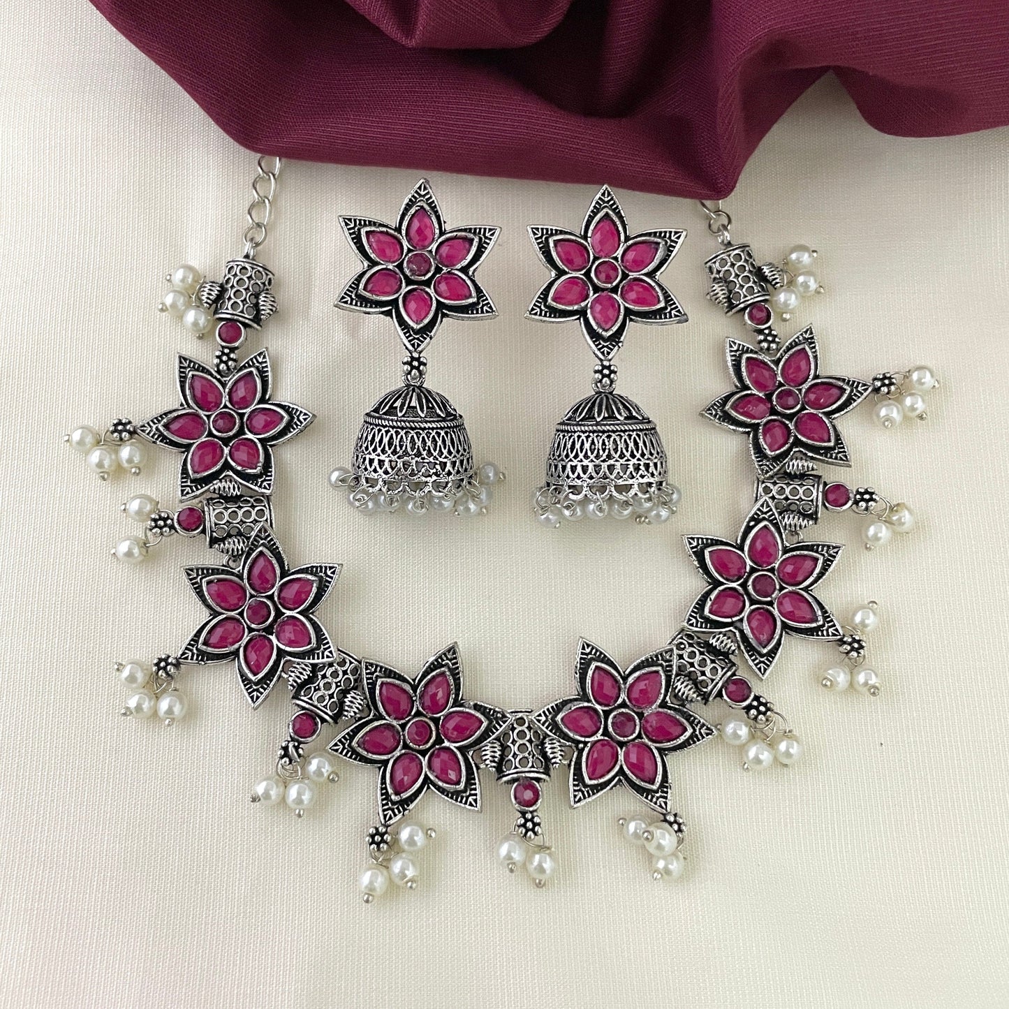 A silver necklace and earring set featuring pink floral designs and pearl accents.