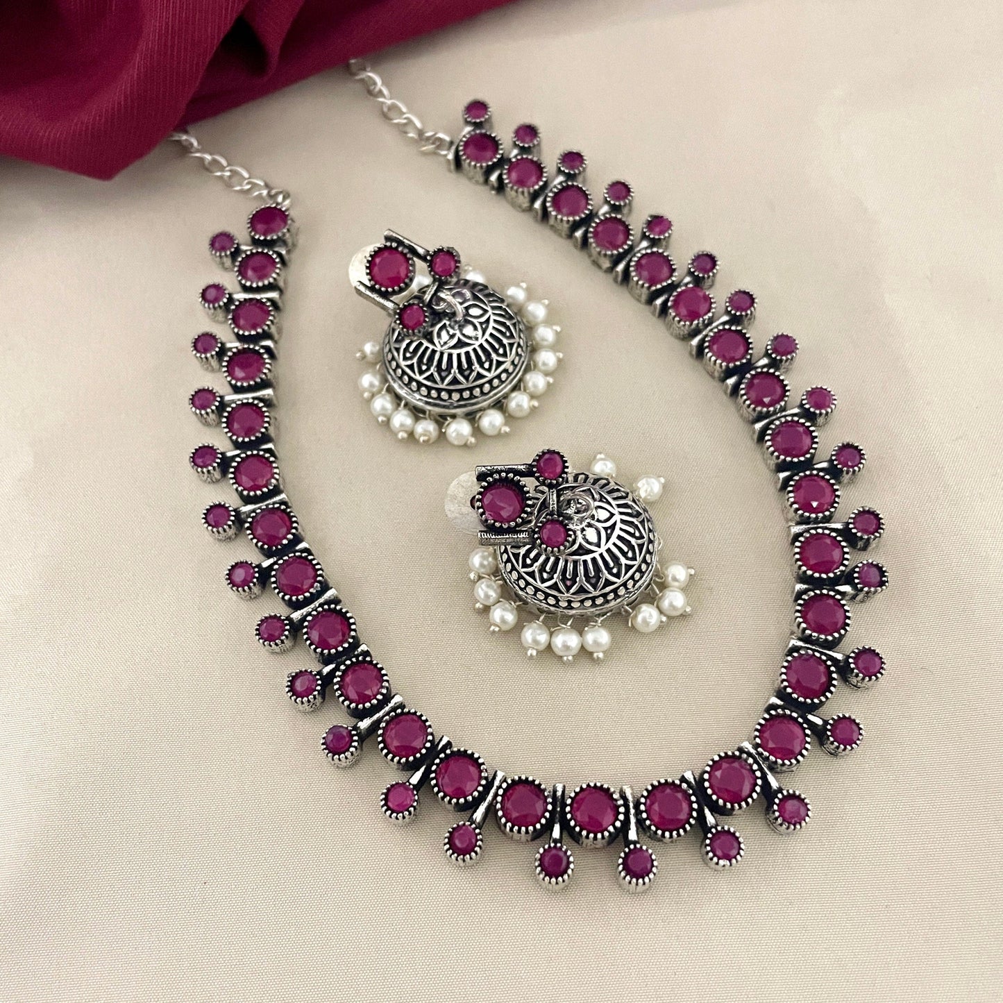 A silver necklace and matching earrings set adorned with pink gemstones and small white pearls.