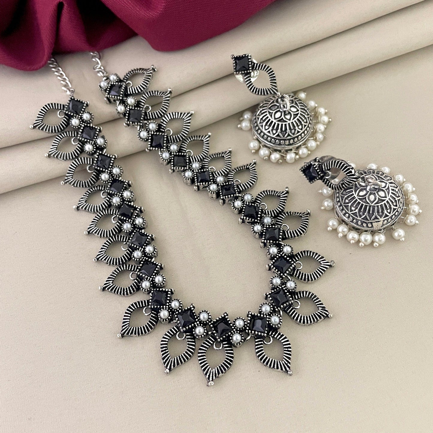Silver necklace with intricate leaf design and matching earrings adorned with pearls.