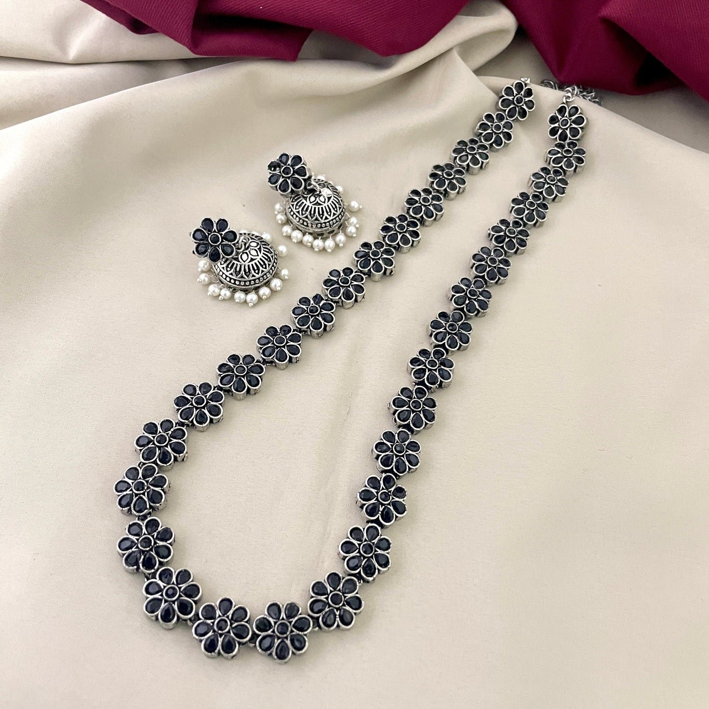 A silver floral necklace with matching earrings featuring intricate designs and pearl accents.