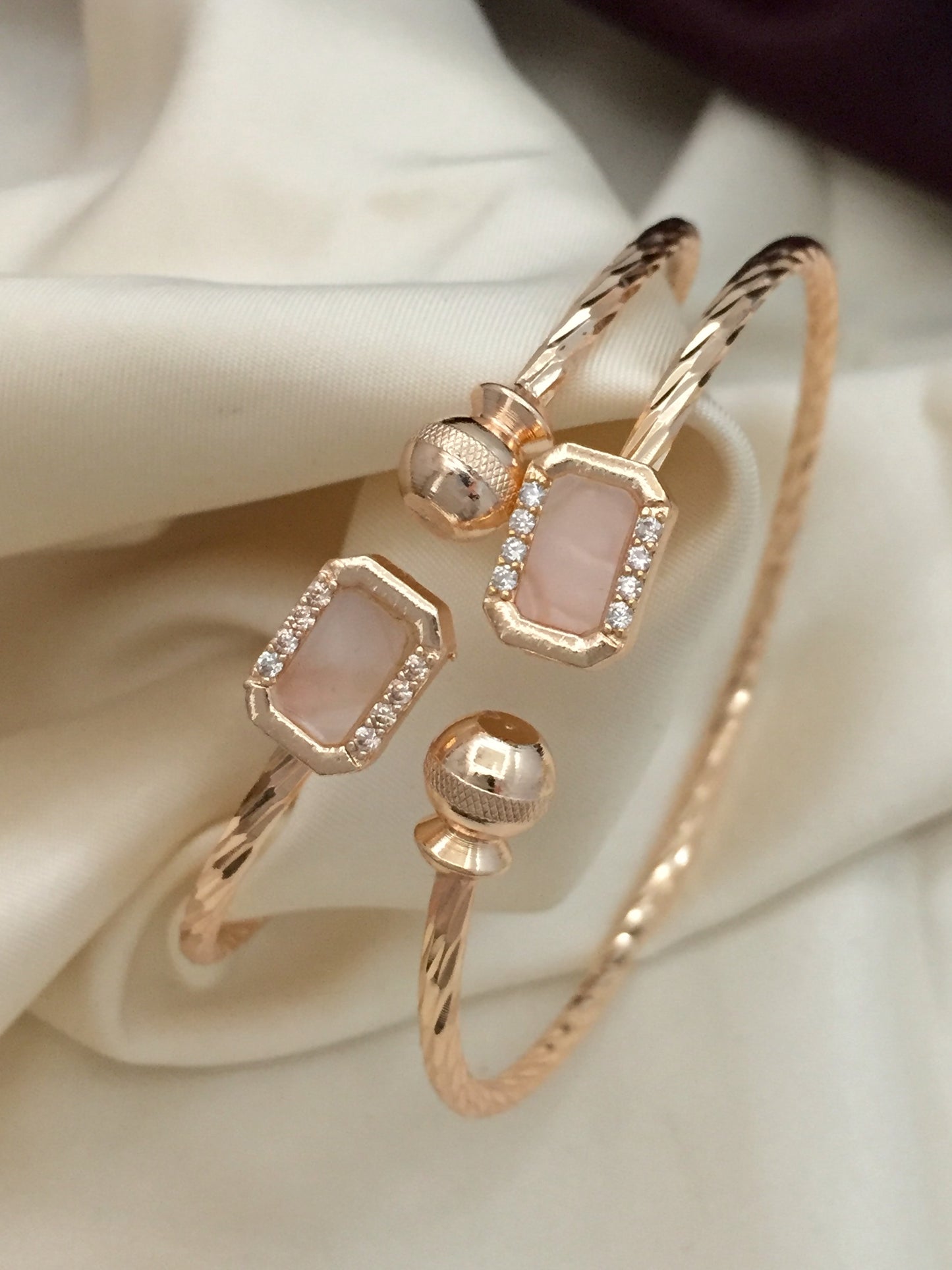 A gold bracelet with two rectangular pink stones and two round gold accents.