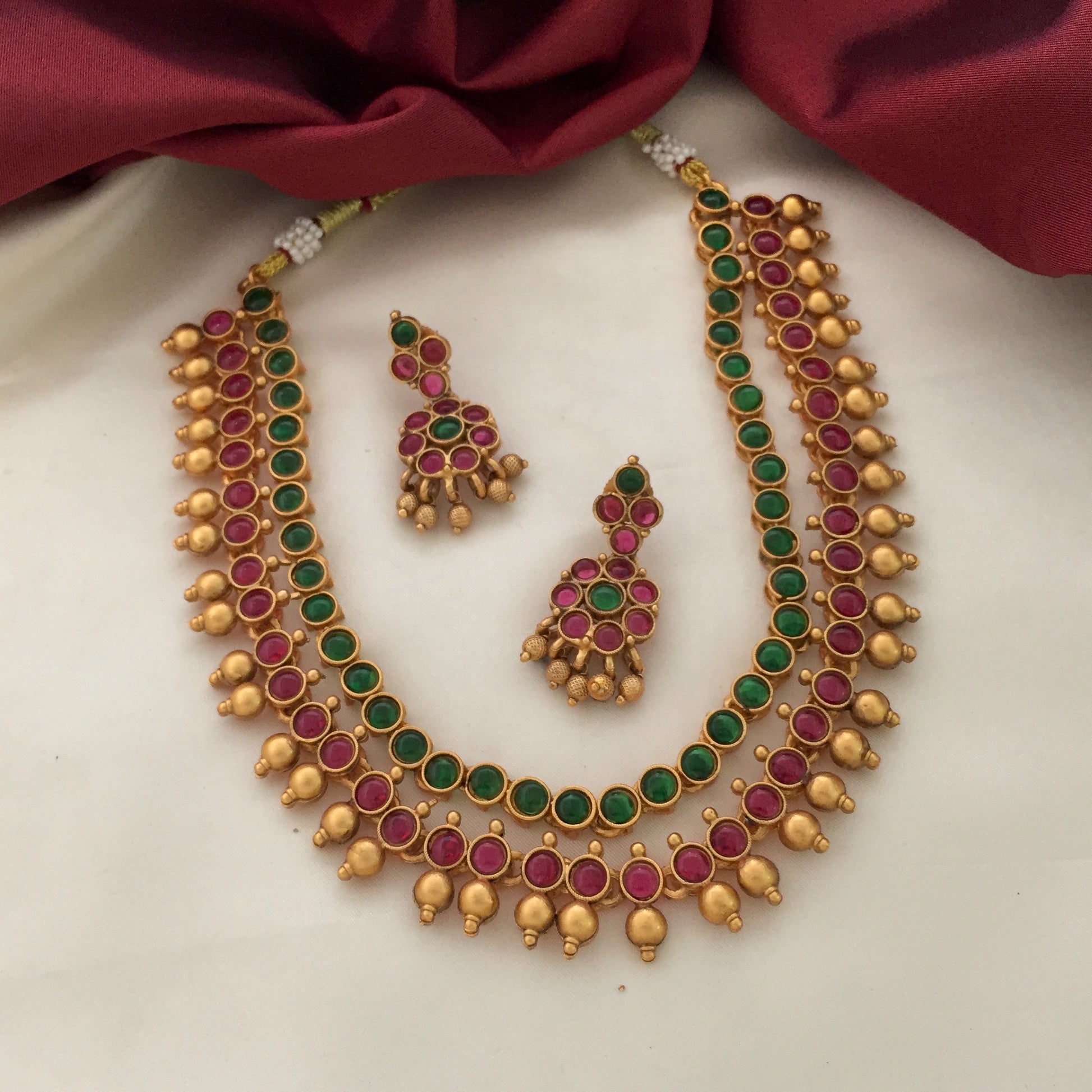 A gold necklace with green and red gemstones, accompanied by matching earrings.