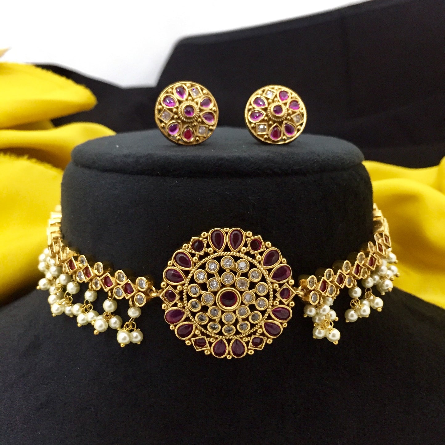 Gold choker necklace with intricate design, featuring red and white stones, and matching earrings.
