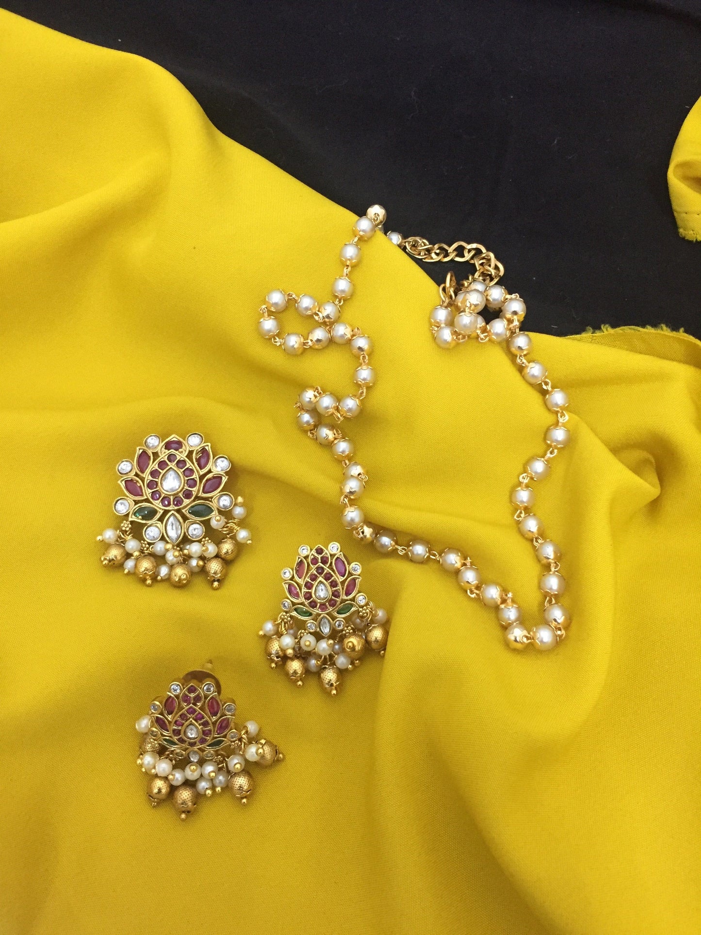 A set of traditional jewelry featuring a pearl necklace and three ornate earrings with gold, red, and green detailing.