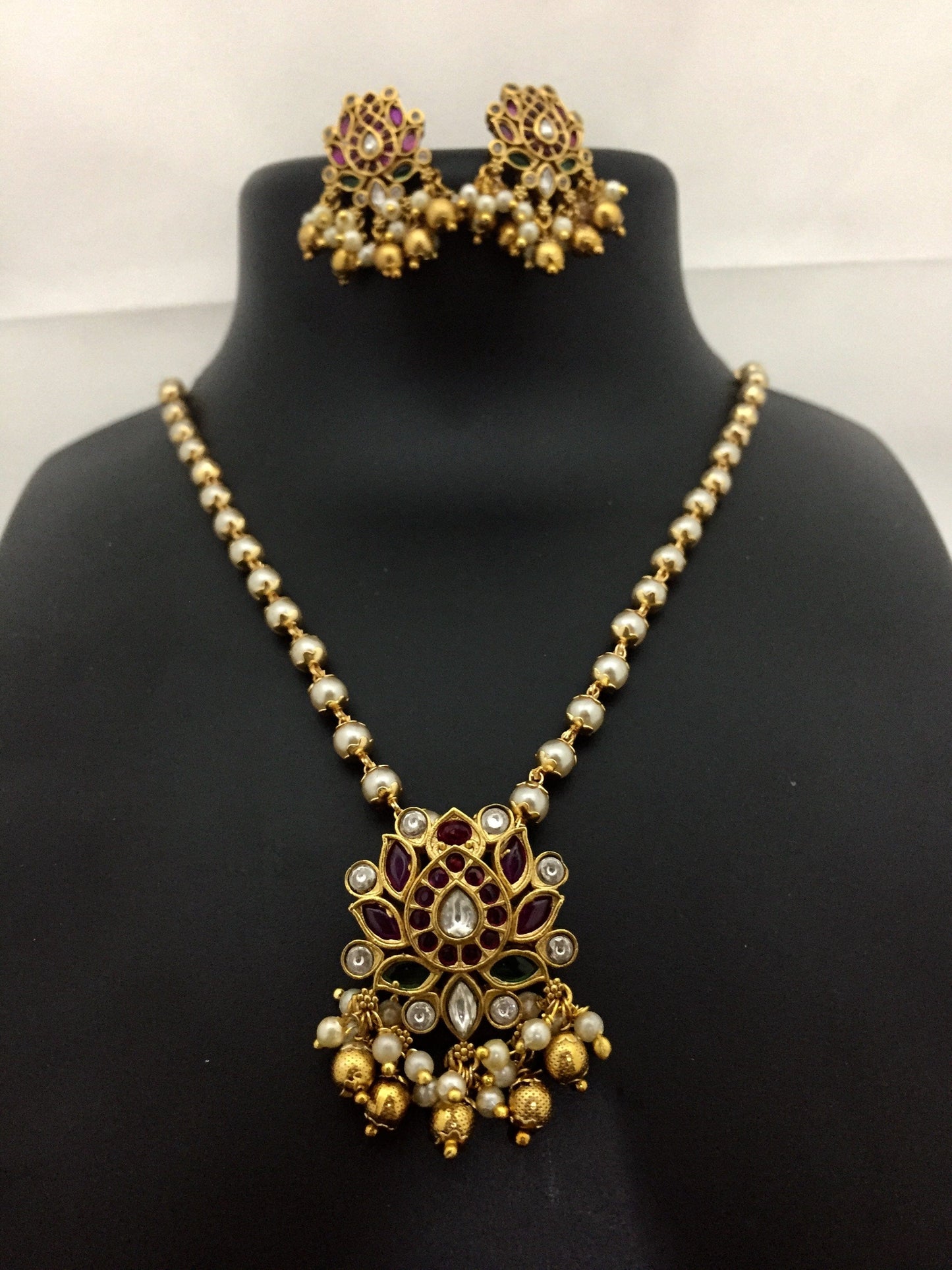 Gold and pearl necklace with matching earrings featuring intricate floral designs and dangling beads.