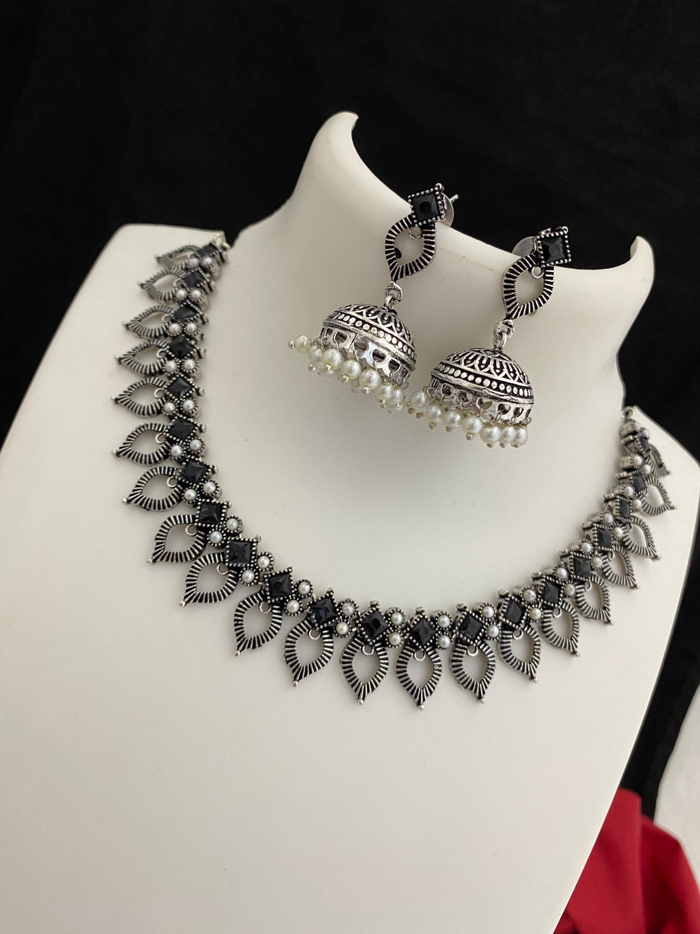 A silver oxidized necklace with intricate leaf-shaped designs and matching jhumka earrings adorned with small white pearls.