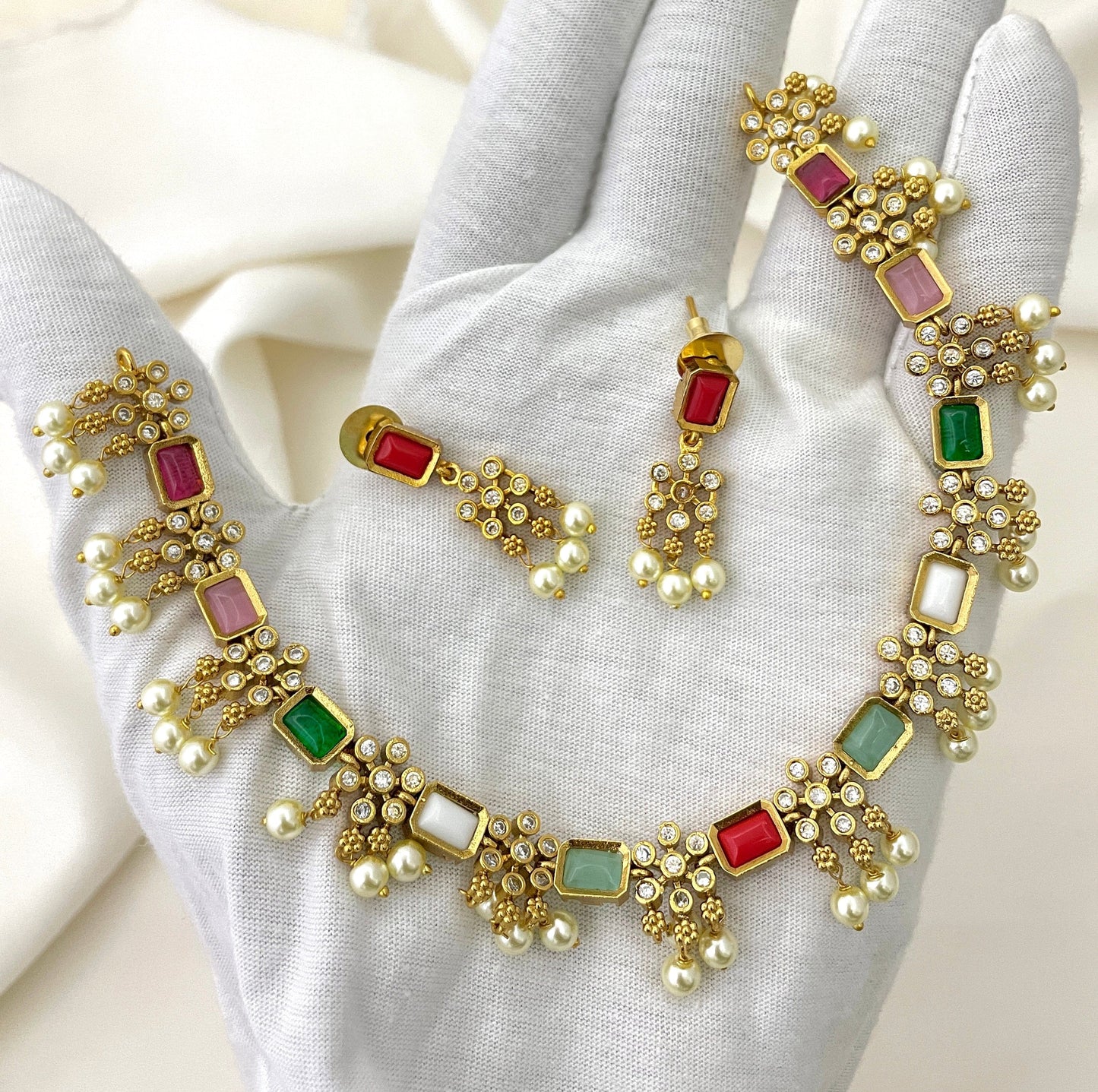 A gold necklace and earring set adorned with multicolored gemstones, pearls, and small white crystals.
