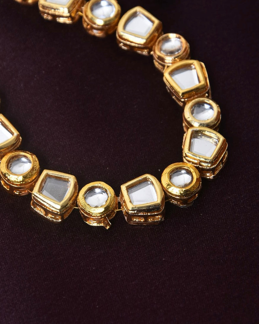 A close-up of a gold necklace with square and round white gemstones.