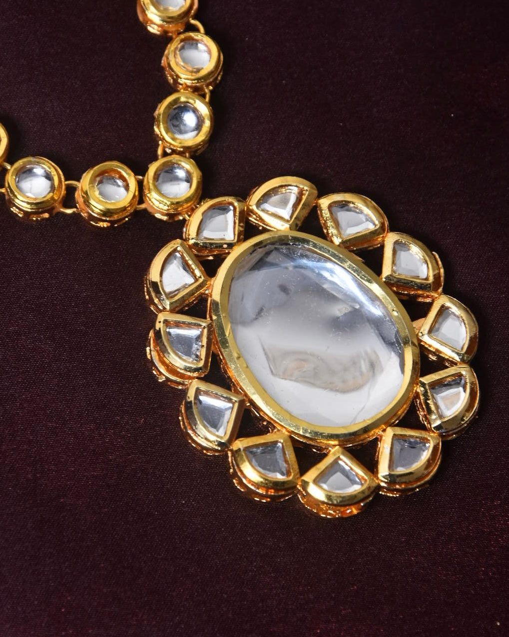 A gold necklace with a large oval-shaped pendant featuring a clear gemstone in the center, surrounded by smaller triangular gemstones.