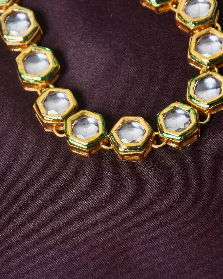 A close-up of a gold necklace with hexagonal-shaped links, each containing a clear gemstone.