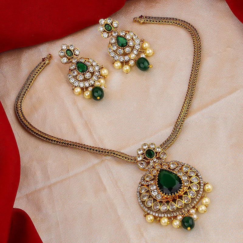 A gold necklace and earring set with green gemstones and pearl accents displayed on a beige fabric background.