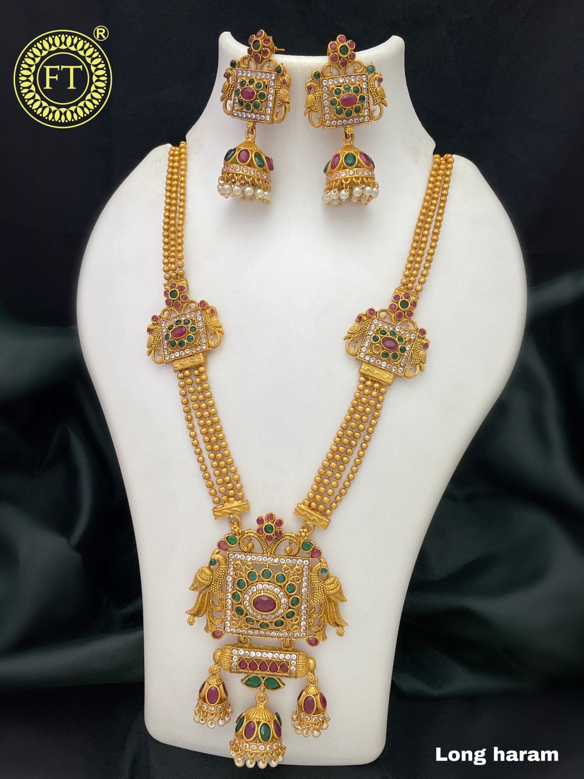 Gold long haram necklace set with intricate designs, featuring red and green gemstones, and matching earrings.