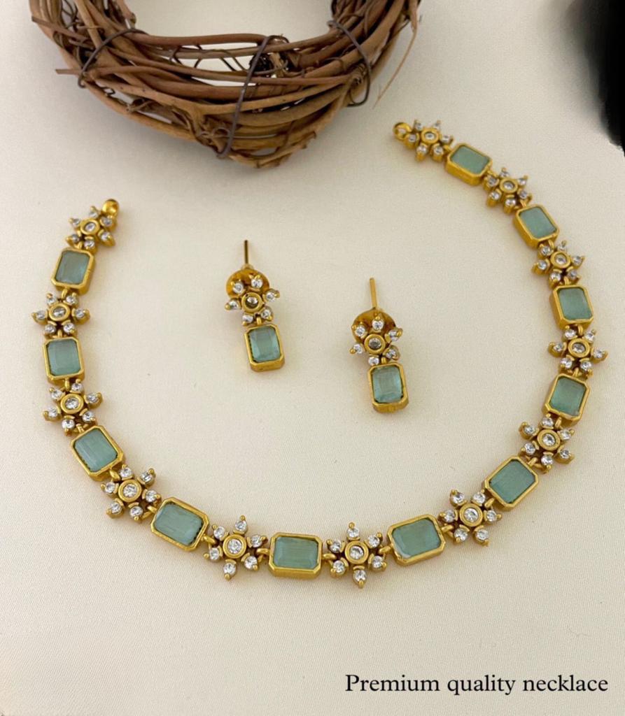 A gold necklace with rectangular green stones and matching earrings.