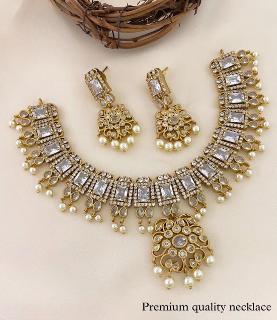 A premium quality gold necklace set with matching earrings, featuring rectangular and round gemstones and pearl accents.
