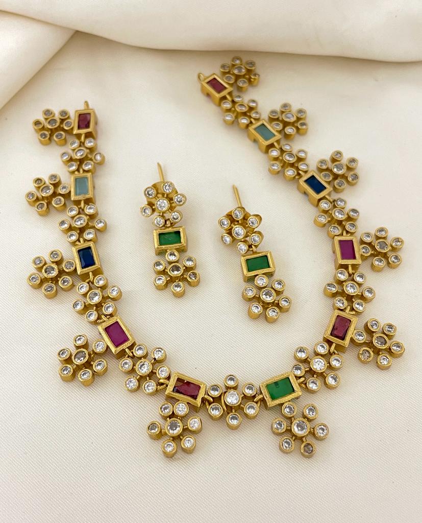 Gold jewelry set with multicolored gemstones and clear crystals, including a necklace and matching earrings.
