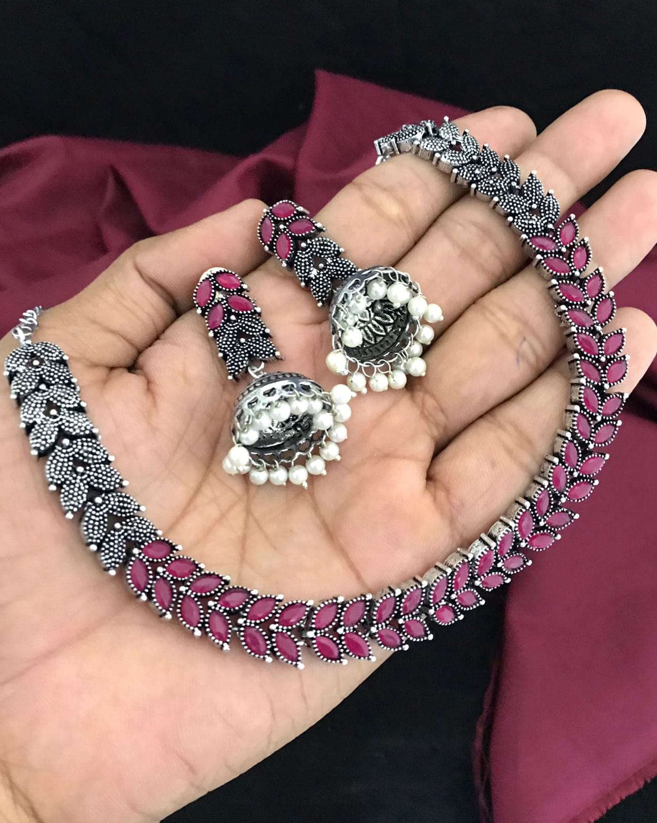 A hand holding a silver necklace with pink leaf-shaped stones and matching earrings with pearl accents.