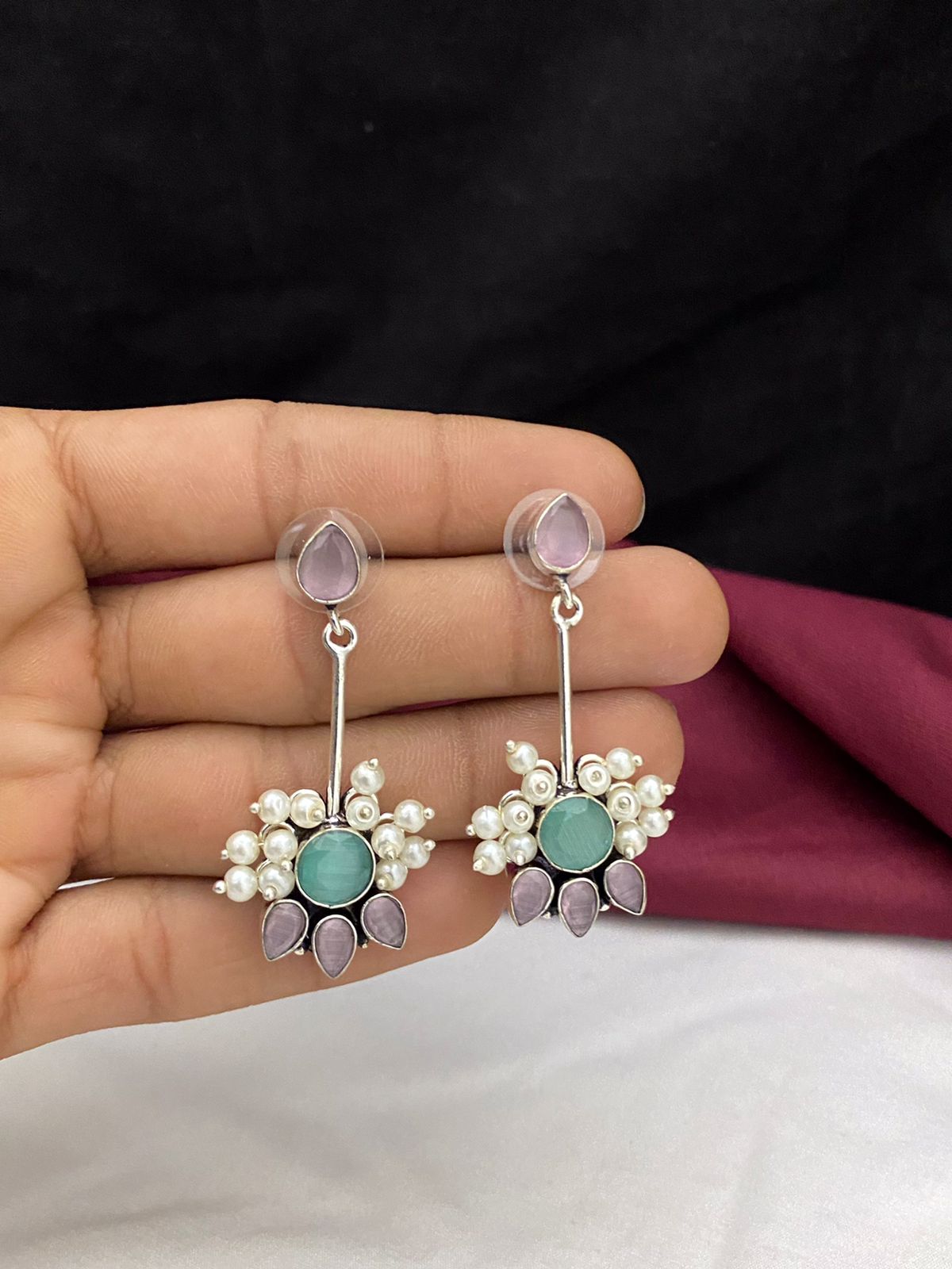 A pair of dangling earrings with purple and green gemstones, adorned with small white pearls.